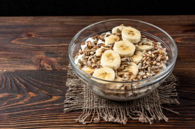 Süzme peynirli yulaf ezmesi, ay çekirdeği ve sarı laleli koyu ahşap zemin üzerinde muz..