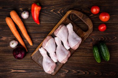 Koyu tahta arka planda çiğ tavuk bacağı ve sebze..