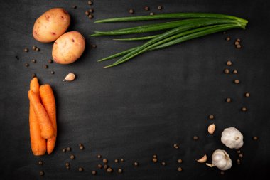 Taze patates, havuç, yeşil soğan, sarımsak ve siyah arka planda kara biber..