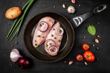 Siyah arkaplanda yeşil soğanlı çiğ tavuk filetosu.