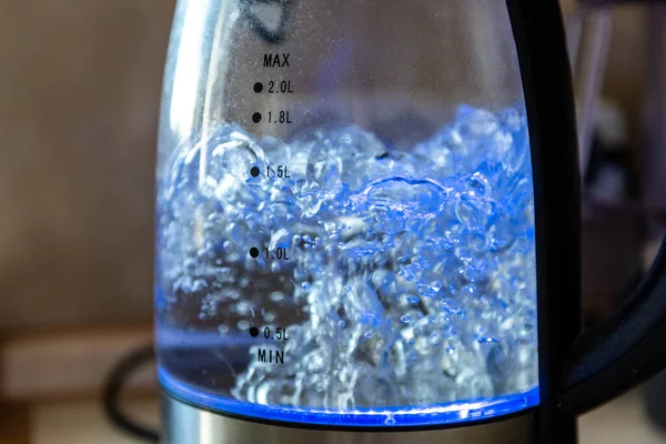 Glass electric kettle with boiling water in kitchen.