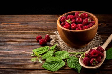 Fresh raspberry in wooden bowl on dark wooden background.