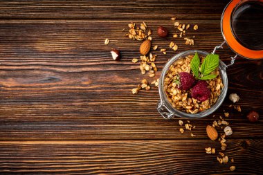Granola in glass jar and raspberry on dark wooden background.