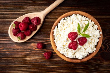 Cottage cheese with raspberry in wooden bowl on dark wooden background.