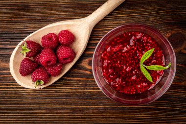 Raspberry jam on dark wooden background.