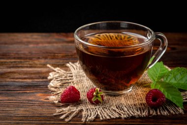 Cup of black tea and raspberry on dark wooden background.