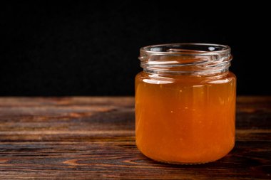 Honey in glass jar and fresh raspberry on dark wooden background.