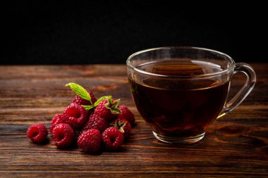 Cup of black tea with raspberry and honey on dark wooden background.