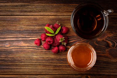 Cup of black tea with raspberry and honey on dark wooden background.