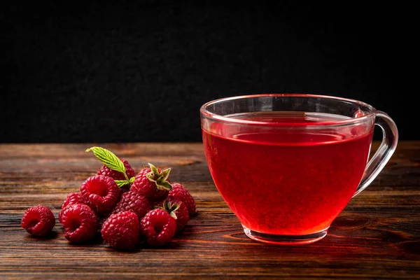 Cup of tea with raspberry on dark wooden background.