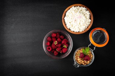 Cottage cheese, granola and fresh raspberry on black background.
