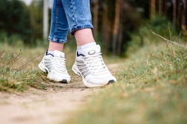 Woman's legs going on field or forest in white sneakers.