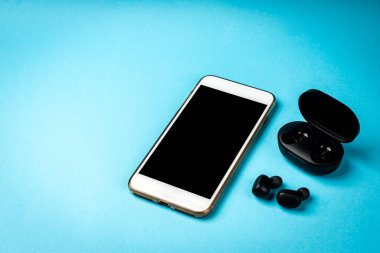 Mavi arka planda siyah kablosuz kulaklık ve beyaz cep telefonu..