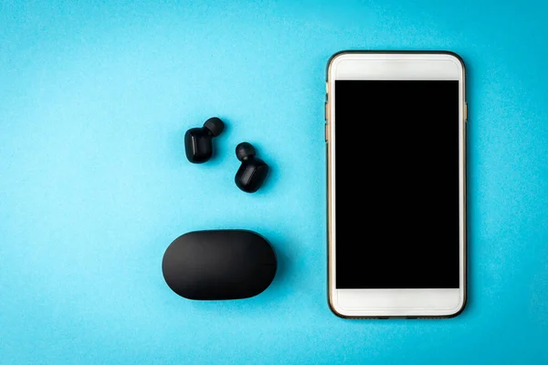 Black wireless headphones and white mobile phone on blue background.