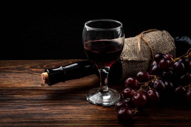Koyu ahşap zemin üzerinde kırmızı şarap ve üzüm..