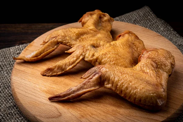 Smoked chicken wings on wooden board on dark wooden background.