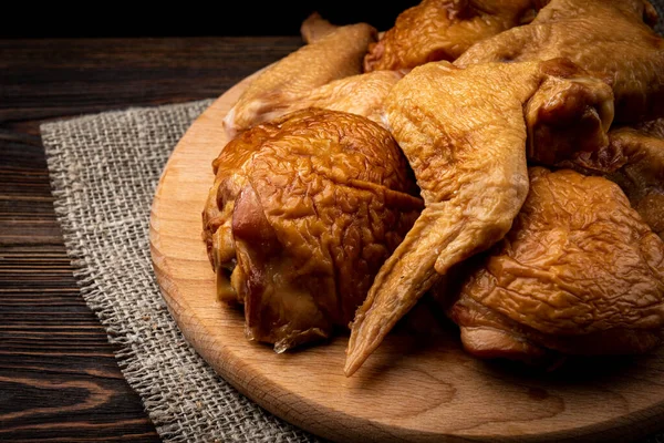 Smoked chicken wings and thigh on wooden board on dark wooden background.