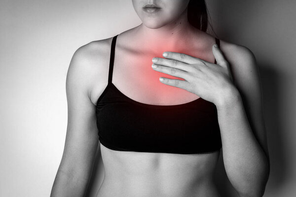 Young woman with pain in chest and lungs on gray background.