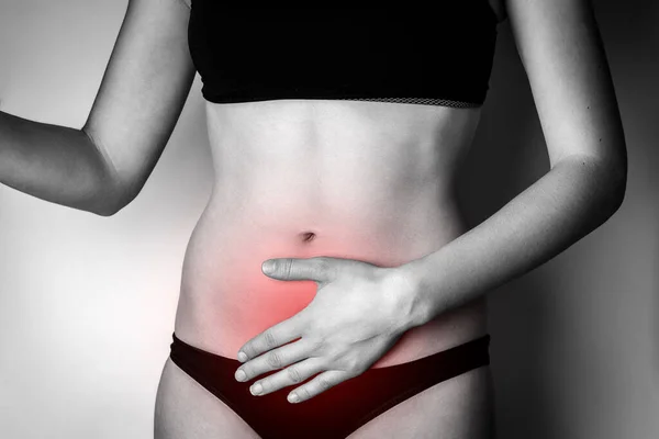 Woman suffering from stomach pain. Young woman with hands holding her crotch lower abdomen gray background.