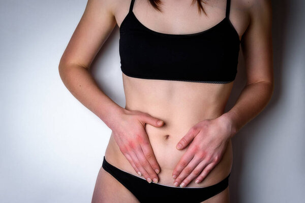 Woman suffering from stomach pain. Young woman with hands holding her crotch lower abdomen gray background.