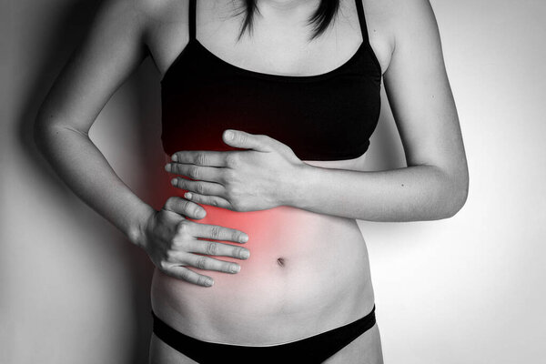 Young woman with pain in liver on gray background.