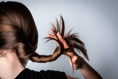 Saçlarının uçlarını gri arka planda tutan genç bir kızın kadın eli..