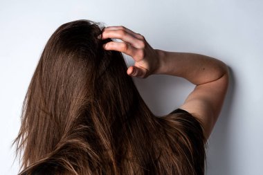 Genç bir kadın gri arka planda parmaklarıyla kafa derisine masaj yapıyor..