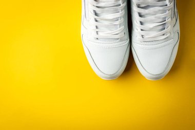 Sarı arka planda beyaz spor ayakkabılar.