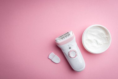 Pembe arka planda elektrikli epilatör ve krem..