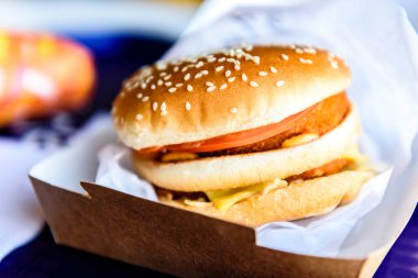 Et ve sebzeli büyük hamburger ve kafenin arka planında patates kızartması. El işi kağıdında ızgarada pişmiş taze burger. Amerikan yemekleri..