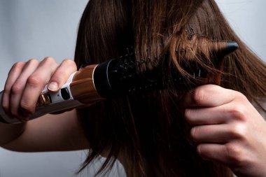 Saç kurutma makinesi olan ve saçını tarayan genç bir kadın..