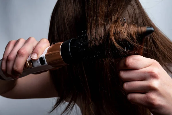 Saç kurutma makinesi olan ve saçını tarayan genç bir kadın..