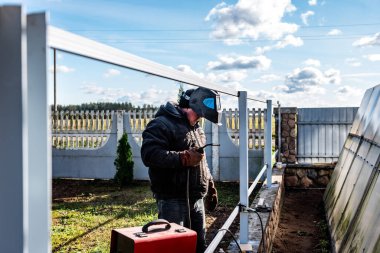 Güvenlik kaskı ve eldiven takan bir kaynakçı metal bir çiti kaynaklıyor..