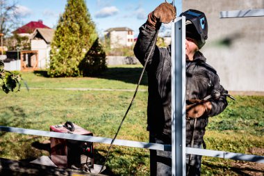 Güvenlik kaskı ve eldiven takan bir kaynakçı metal bir çiti kaynaklıyor..