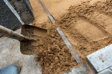 İşçi kaldırım döşemeleri için kum yatağını düzgünce tarıyor.