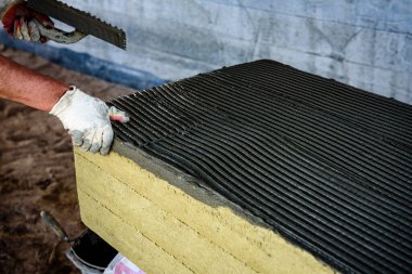 Ev yalıtımı için mineral yününe yapıştırıcı süren malalı işçi eli. Ev ısıtma enerjisinden tasarruf etmek için fiberglas levhalar.