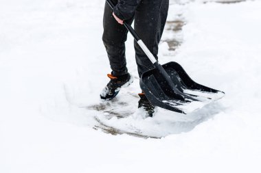 Kaldırımdan kar temizleyen ve kar küreği kullanan bir kadın..