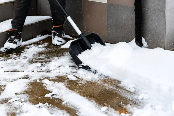 Woman cleaning snow from sidewalk and using snow shovel.