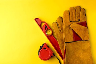 Sarı inşaat koruyucu eldivenler, kırmızı bina seviyesi ve sarı arka planda şerit ölçü..