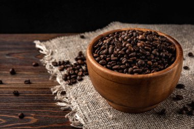 Koyu ahşap arka planda, tahta kasede kahve çekirdekleri..