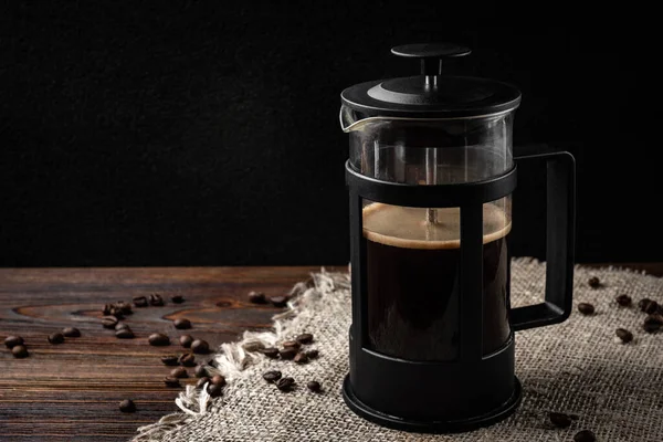 Coffee in french press and coffee beans on dark wooden background.