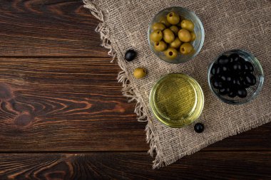 Koyu ahşap zemin üzerinde yeşil ve siyah zeytin yağı. Üst görünüm.