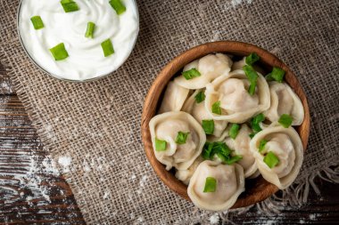 Rus pelmeni ya da ekşi kremalı etli köfte ve ahşap zemin üzerinde yeşil soğan..