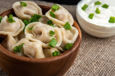 Rus pelmeni ya da ekşi kremalı etli köfte ve ahşap zemin üzerinde yeşil soğan..