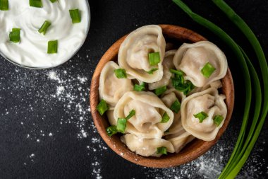 Ahşap kasede köfte, ekşi krema ve siyah arka planda yeşil soğan..