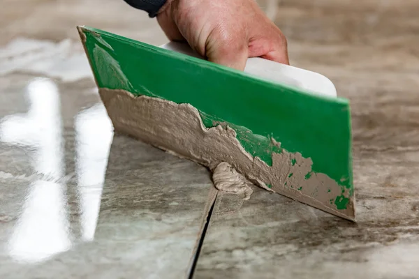 Grouting ceramic tiles. Tilers filling the space between tiles using a rubber trowel.