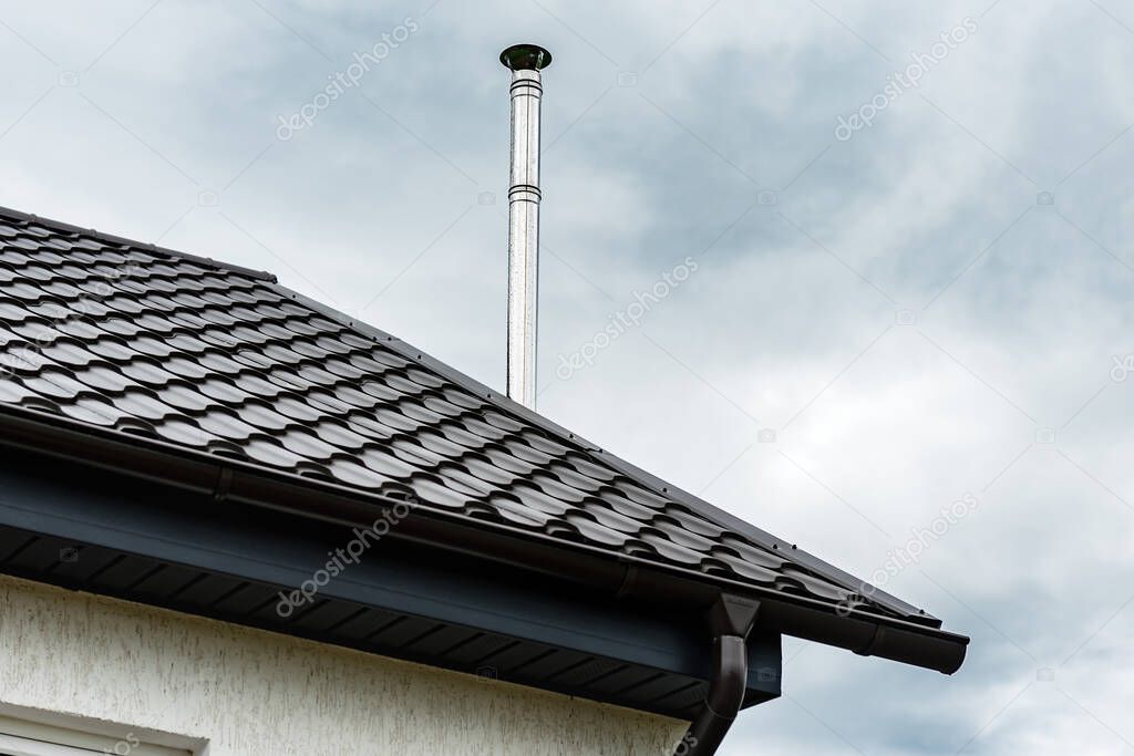 Silver chimney pipe on metal roof of house.