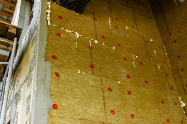 Sheets of green mineral wool are attached to the wall with dowels with red plastic caps. Construction phase. 