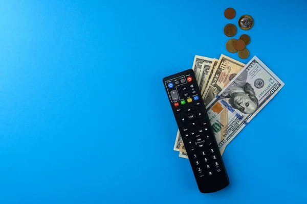 TV remote controller and money on blue background.