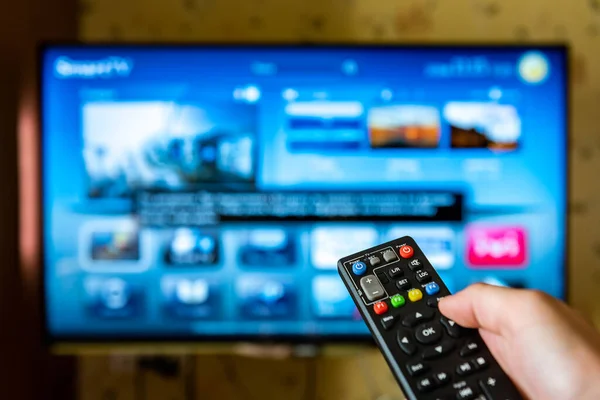 Hand holding and pressing TV remote control.